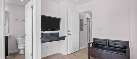 Un bagno moderno con WC, lavandino e specchio. C'è una TV montata a parete e una panca nell'angolo.