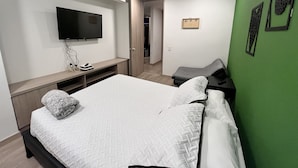 Et moderne hotelværelse med en stor seng, et vægmonteret fladskærms-TV, et skrivebord med stol, og en accentvæg i grøn.