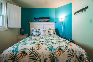 Une chambre à coucher comprenant un lit, une table de chevet, une étagère fixée au mur ornée d’un motif représentant un poisson, et une lampe fixée au mur.