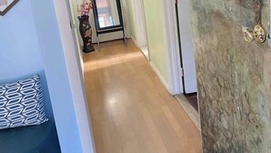 A hallway with a wooden floor, a door with a mirror, and a wall with a decorative piece. - Spacious, comfortable rooms near beach & Newport (Middletown)