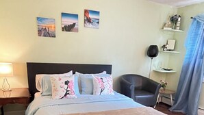 A neatly arranged bedroom with a large bed, a chair, a nightstand, and wall art. - Spacious, comfortable rooms near beach & Newport (Middletown)