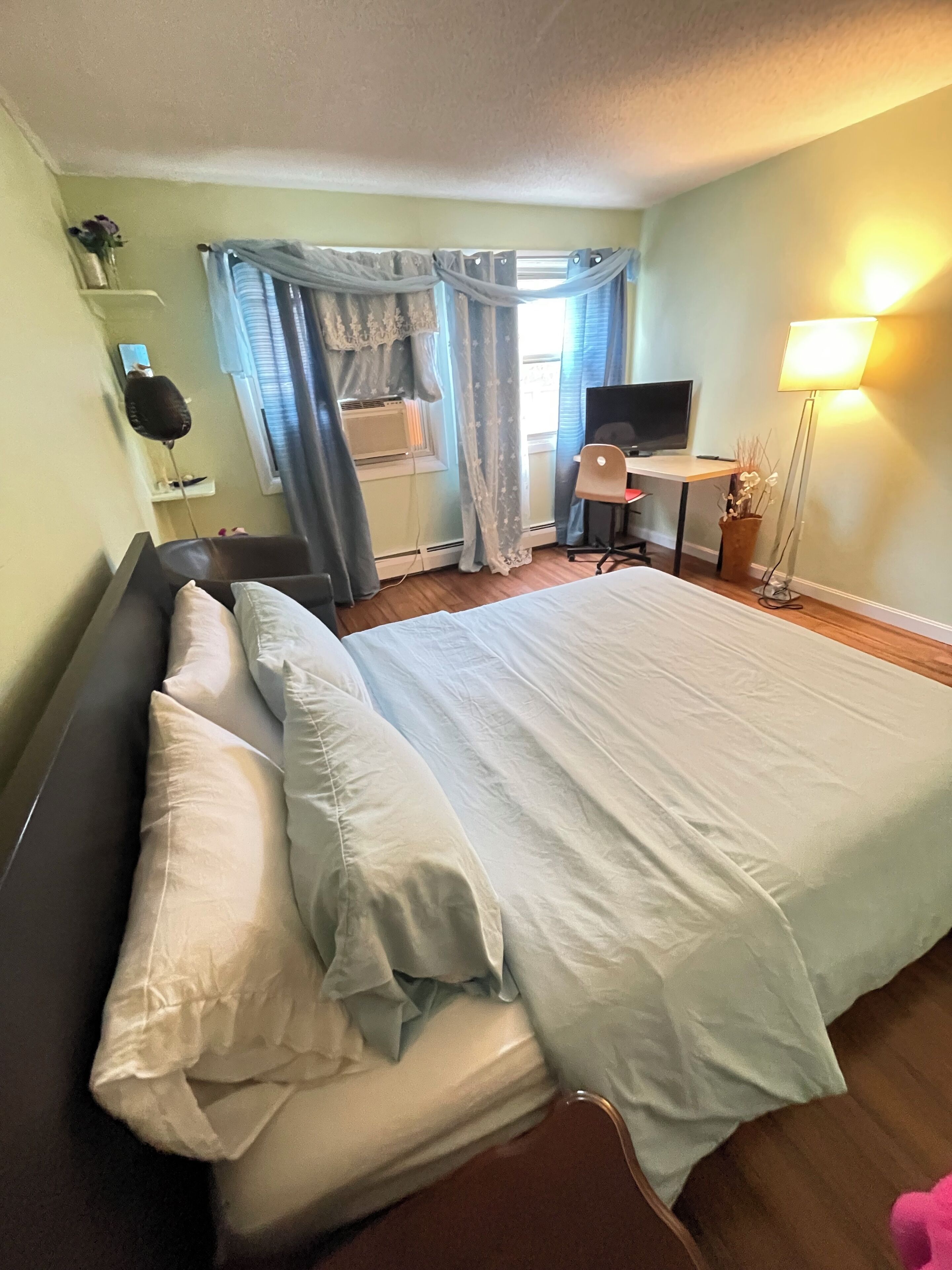Una habitación de hotel con cama, escritorio, silla, televisor y lámpara.
