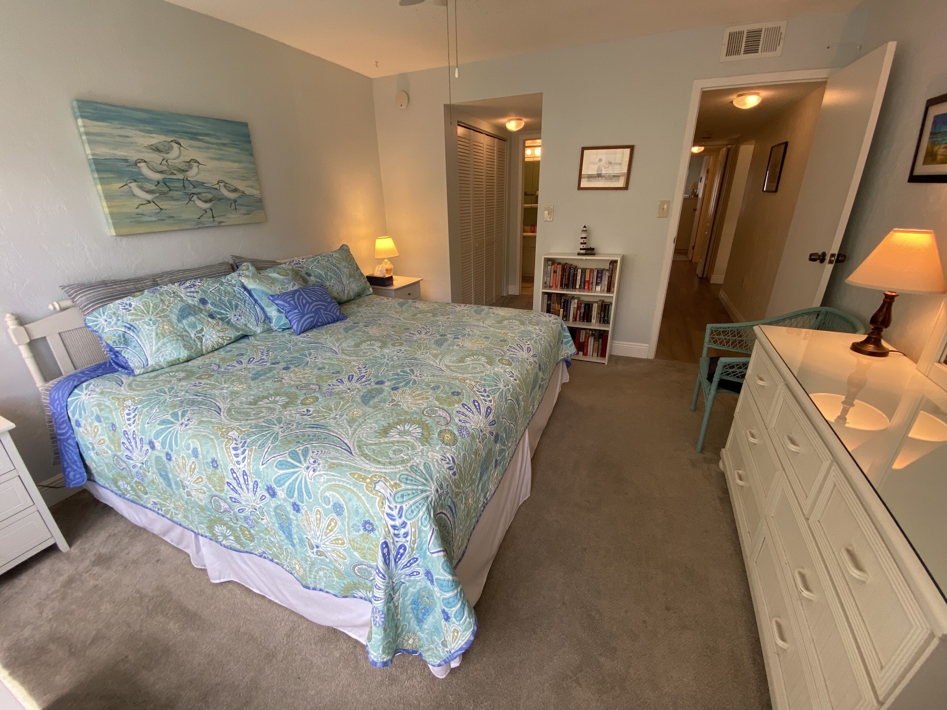 Une chambre à coucher comprenant un lit, des tables de chevet, une commode, une bibliothèque et un tableau accroché au mur.