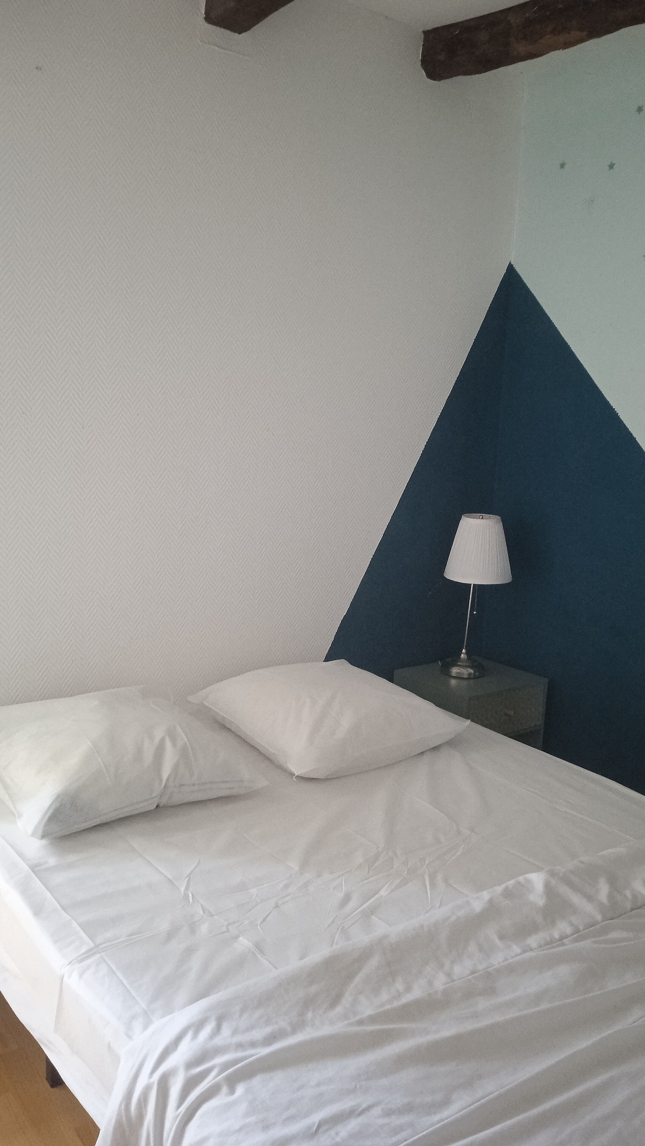 Un lit avec une literie et des oreillers blancs, une table de chevet avec une lampe, et un mur d’accent bleu.