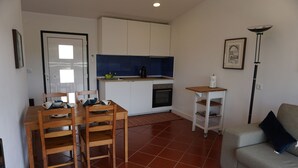 A compact living space with a kitchenette, a dining area with wooden furniture, a sofa, and a floor lamp.