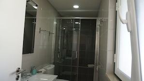 A bathroom with a glass shower enclosure, a white sink, and a toilet.