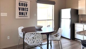 Un coin repas avec une table et des chaises, une cuisine équipée d’un réfrigérateur, et un panneau sur lequel on peut lire : « AMBIANCE POSITIVE SEULEMENT ».