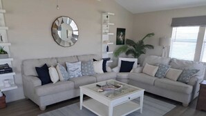 Un salon moderne avec un canapé d’angle beige, une table basse blanche et un grand miroir au mur.