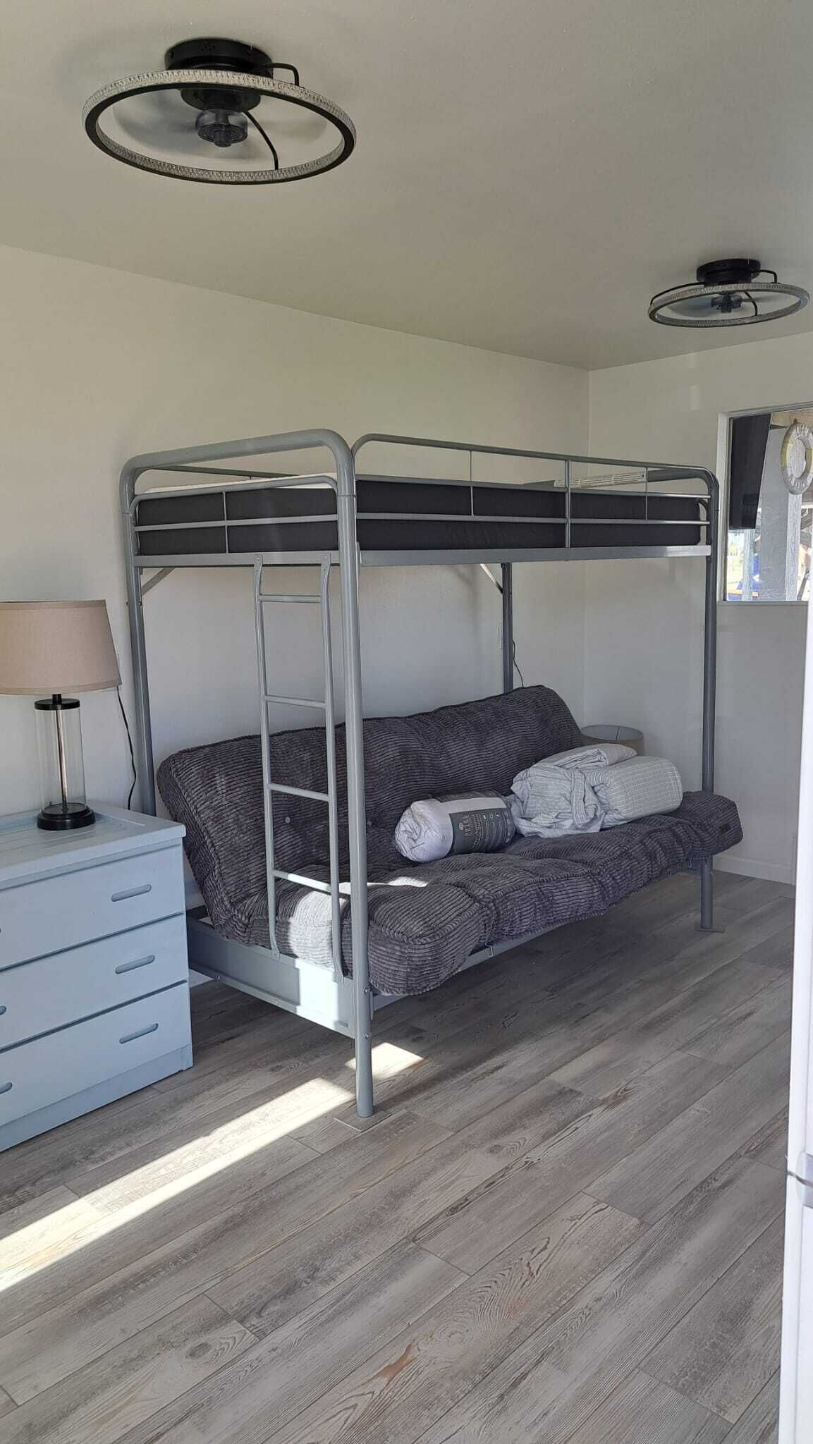 A bunk bed with a metal frame, a bedside table with a lamp, and a dresser with drawers.