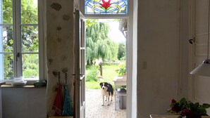A room with a wooden ceiling, a stained glass window, a dog outside, and a tiled floor. - Attractive holiday home in central France (Tranzault)
