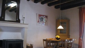 A dining area with a wooden table, chairs, a hanging light fixture, a fireplace, and a framed picture on the wall. - Attractive holiday home in central France (Tranzault)