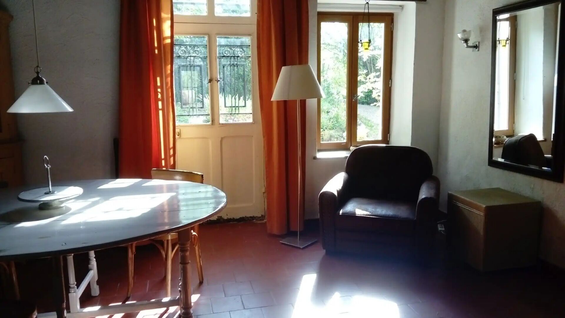 Una habitación con una mesa redonda de comedor, una silla, un sofá, un pequeño armario y una ventana con cortinas.