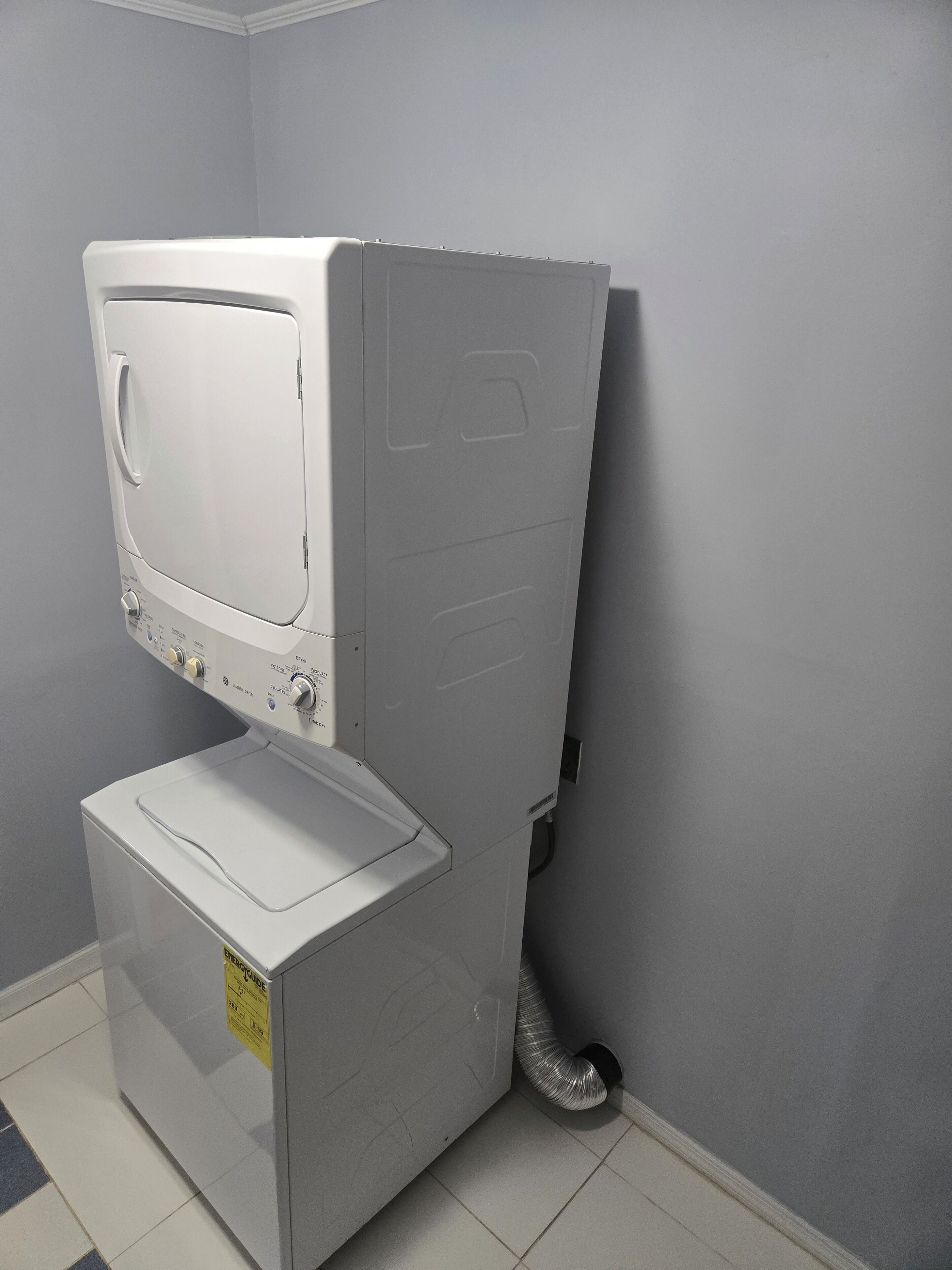 Een kleine, witte wasruimte met een verticaal gestapelde wasmachine en droger.