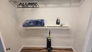 Un armario con estantes para colgar ropa, un aspirador y una plancha pequeña.