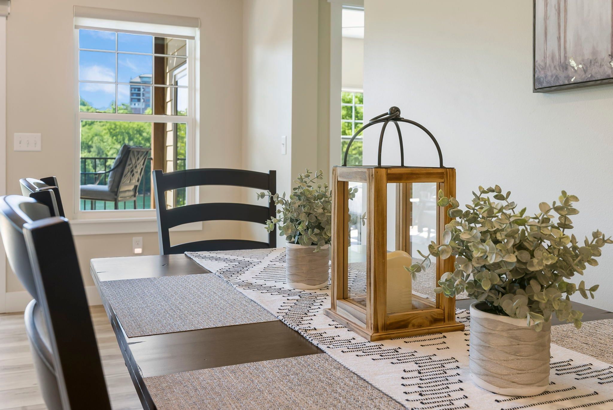 A dining area with a table, chairs, a rug, a lantern, and a potted plant.
