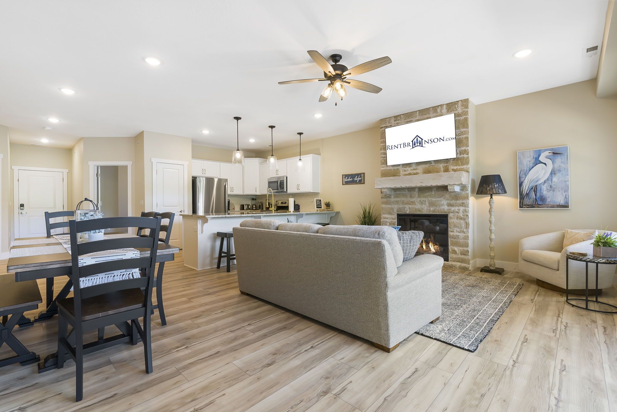 A modern living room with a sofa, dining table, and chairs, a kitchen in the background, and a fireplace with a sign above it.
