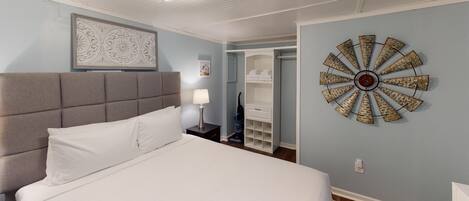 A bedroom with a large bed, a headboard, a wall clock, and a closet with shelves.
