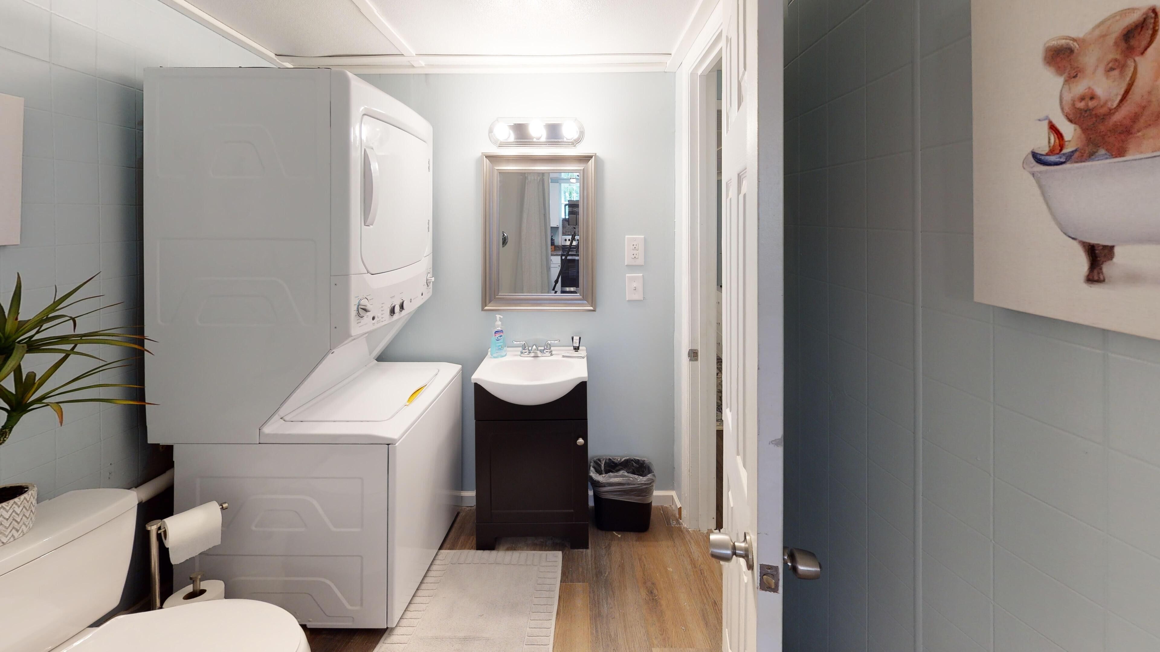 A compact bathroom with a washing machine, sink, and a mirror with lights.