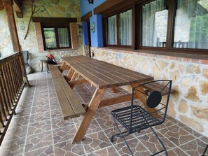 A wooden picnic table with benches, a metal chair, and a stone-tiled floor. - Casa Trasgu Para 8 Personas en Tornín, Cangas de Onís (Asturias)