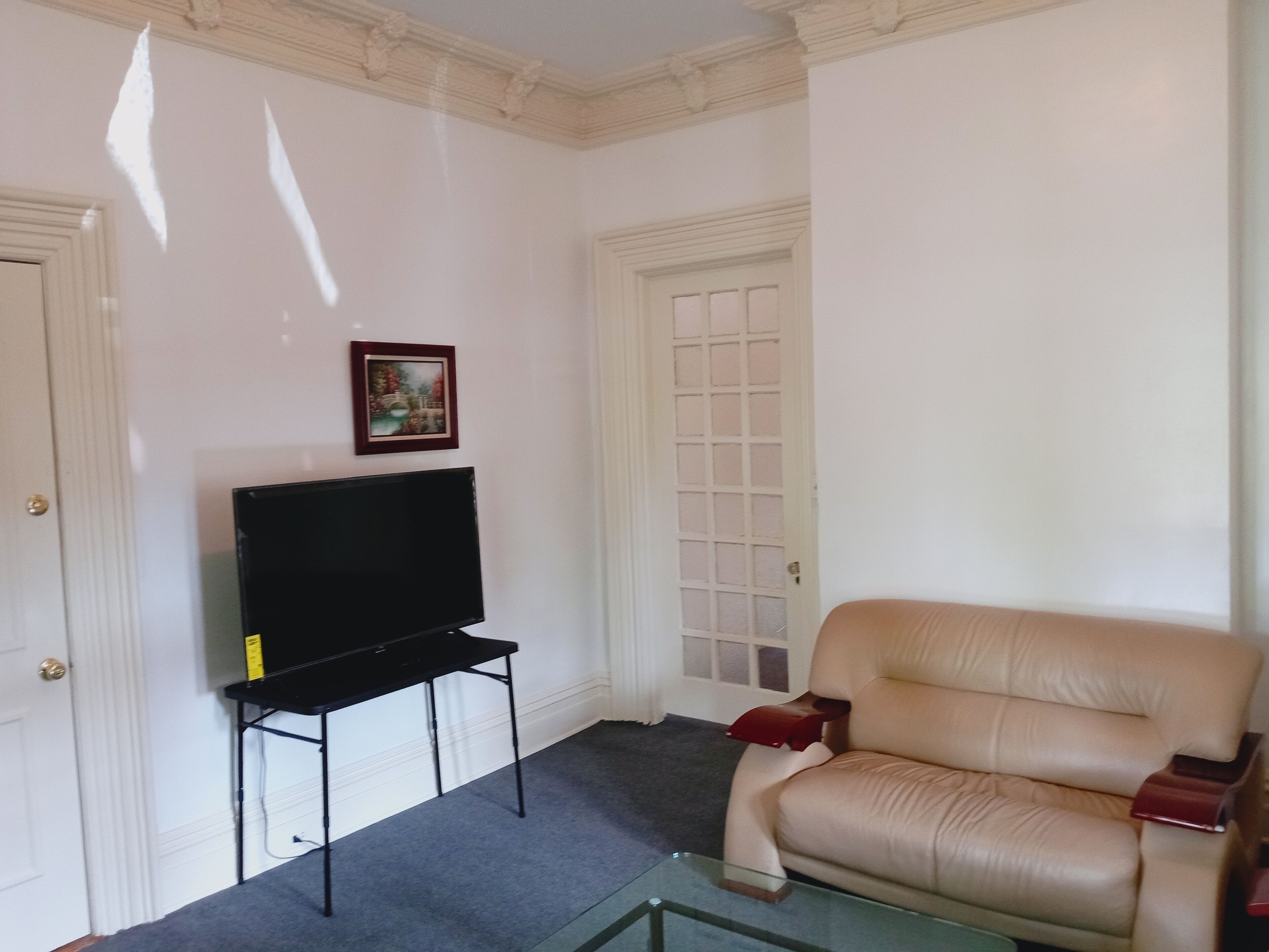 Een woonkamer met een flatscreen televisie op een standaard, een beige bank en een glazen salontafel.