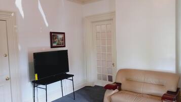 Een woonkamer met een flatscreen televisie op een standaard, een beige bank en een glazen salontafel.