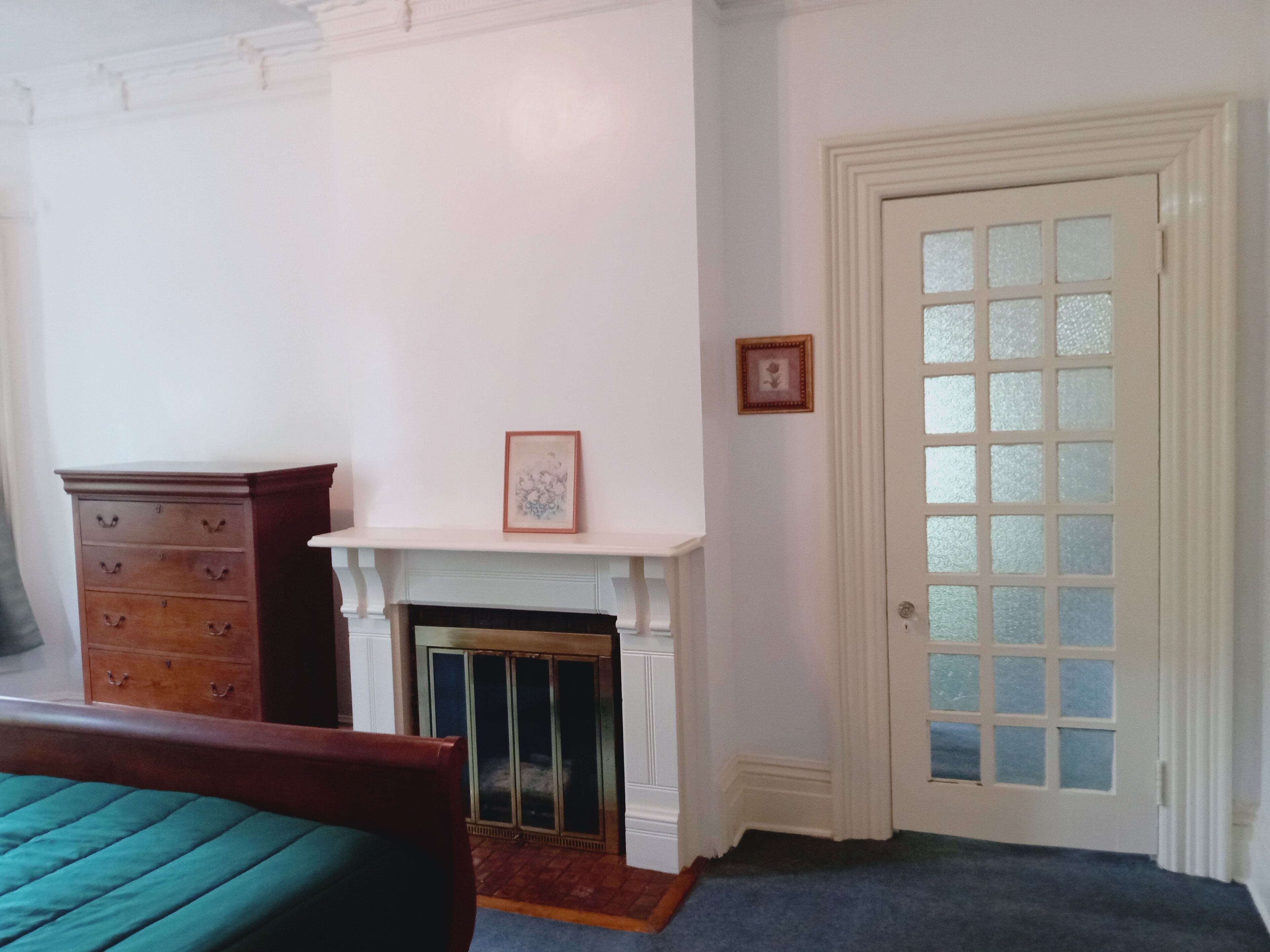 A room with a fireplace, a wooden dresser, a bed, and a door with glass panels.