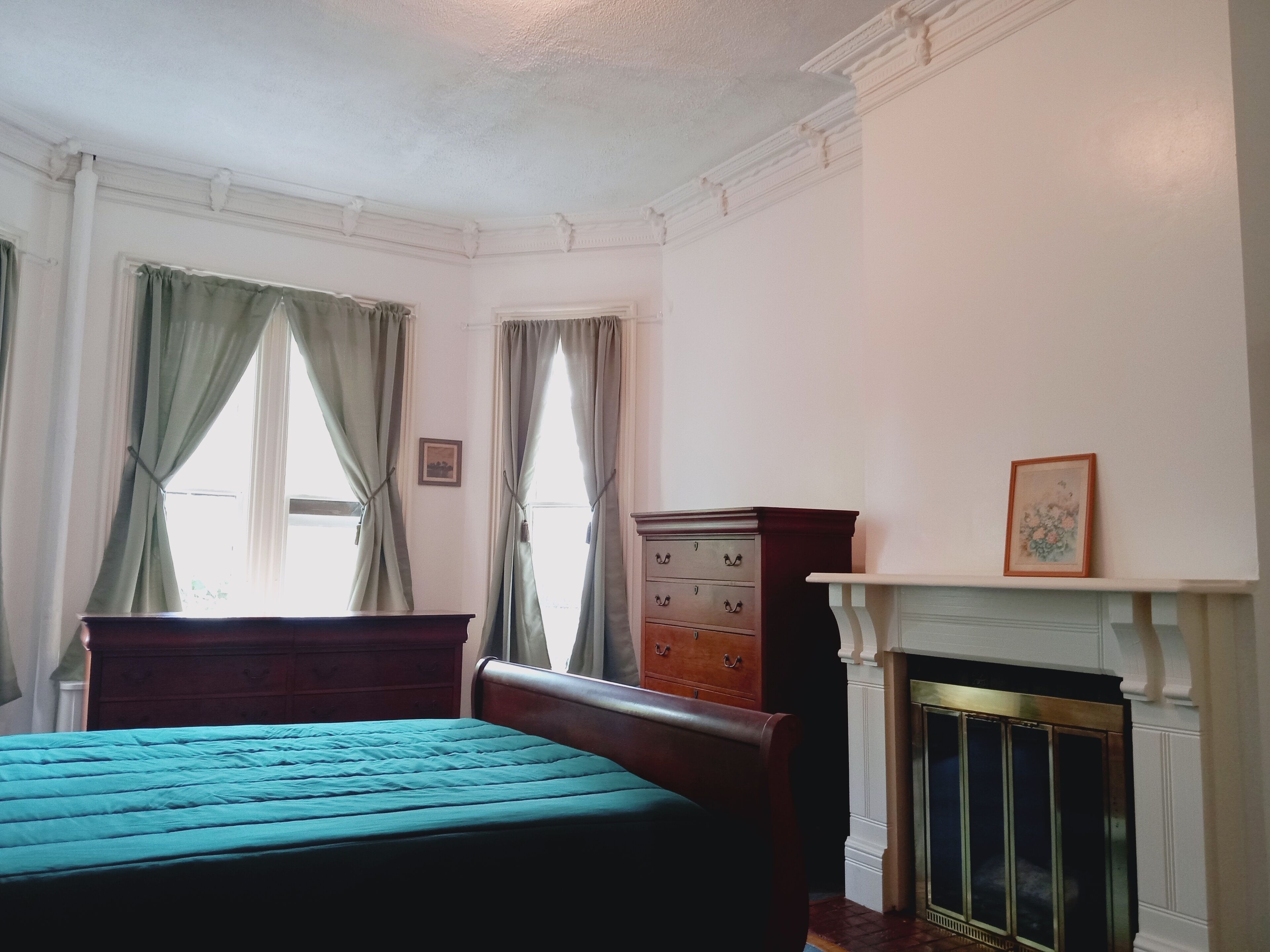 Une chambre à coucher avec un lit, une commode, une cheminée et des rideaux.