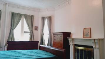 Une chambre à coucher avec un lit, une commode, une cheminée et des rideaux.