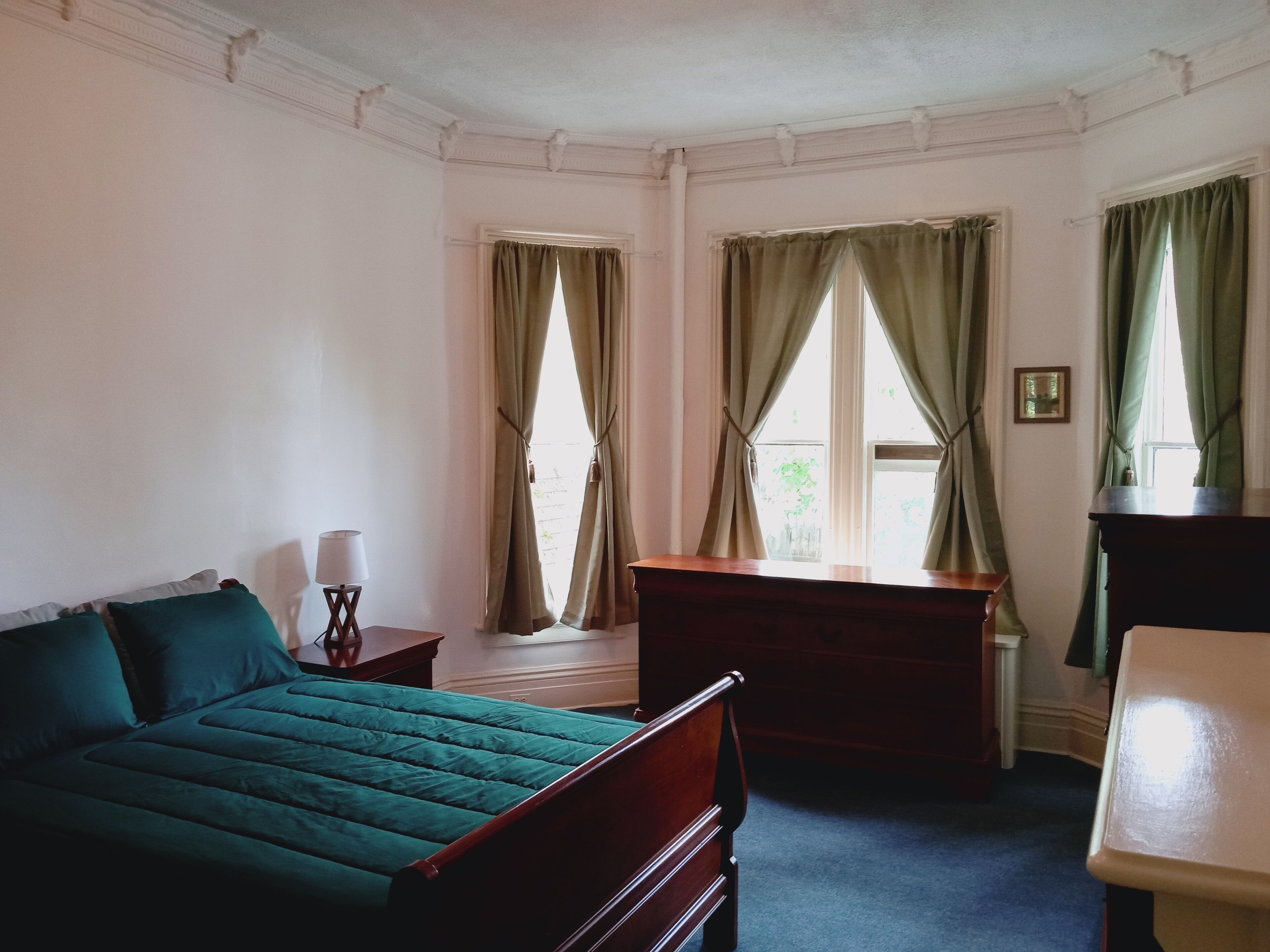 Ein Schlafzimmer mit einem Bett, einem Schreibtisch, einem Stuhl und einem Fenster mit Vorhängen.
