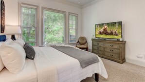 A bedroom with a bed, a dresser, a television, and large windows.