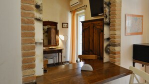 Une pièce avec une arche en briques, une table en bois, deux chaises blanches, un téléviseur et une carte accrochée au mur.