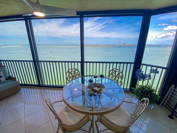A balcony with a glass table and chairs, overlooking a body of water.