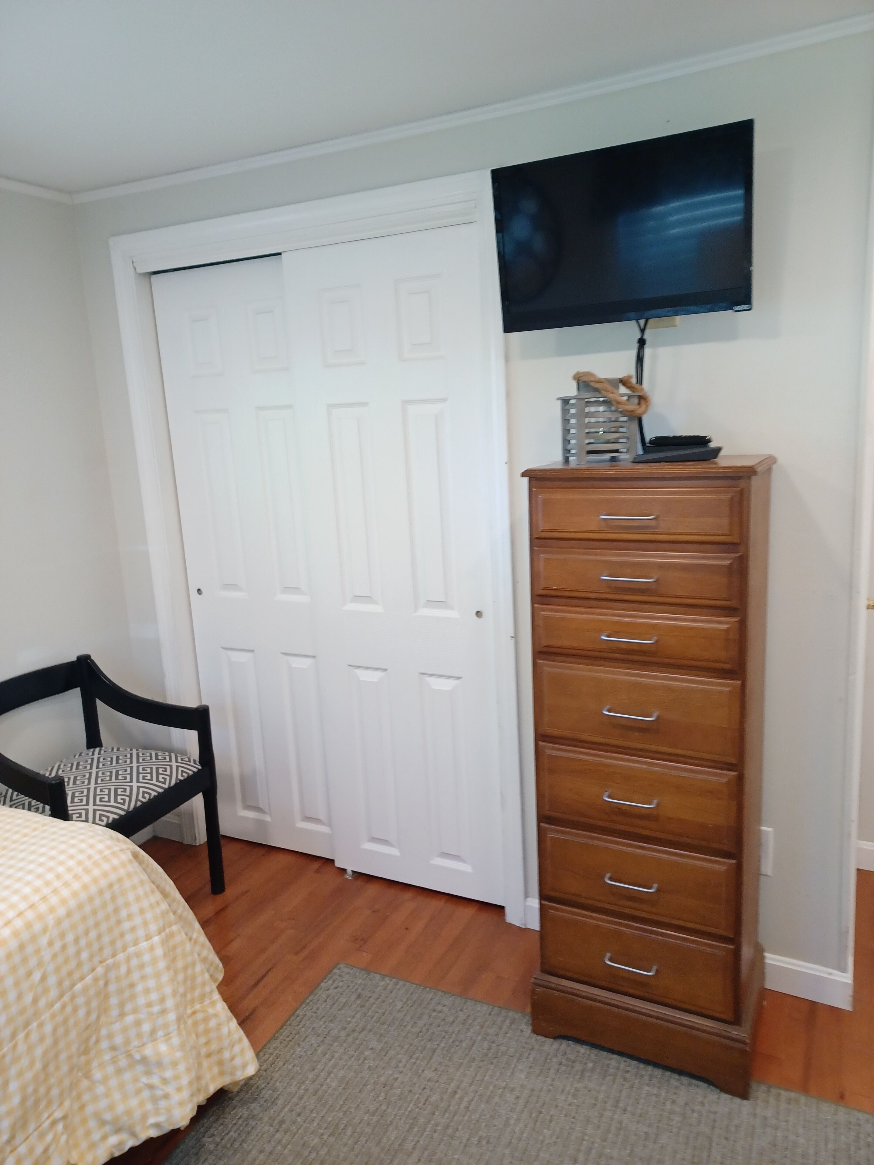 Un dormitorio con una cama, un aparador, una silla, un televisor en la pared y una puerta blanca.
