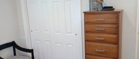 Un dormitorio con una cama, un aparador, una silla, un televisor en la pared y una puerta blanca.