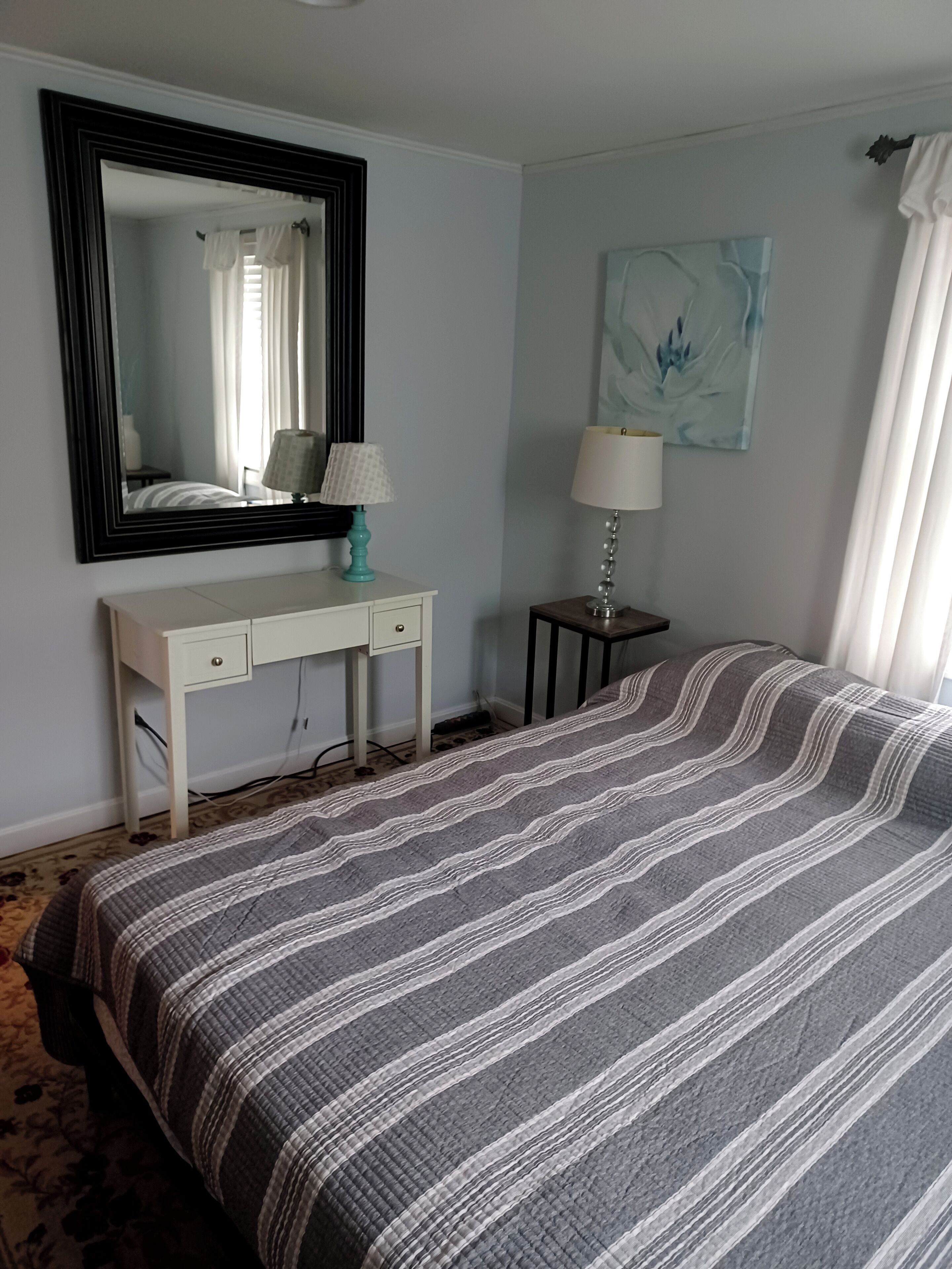 Ein Schlafzimmer mit einem Bett, einem Schreibtisch, einem Spiegel und einer Lampe.