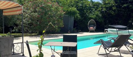 A poolside area with a table and chairs, a covered seating area, and a potted plant.