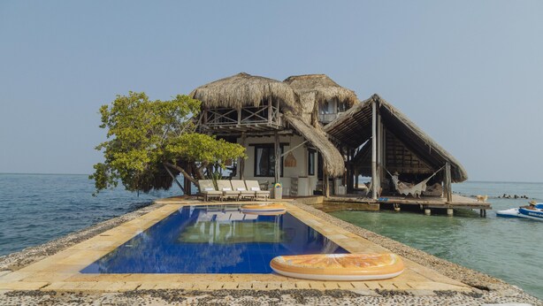 Un bungalow sur pilotis doté d’une piscine, de chaises longues et d’une structure au toit de chaume.