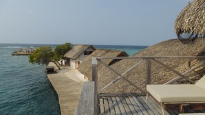 Bungalows sur pilotis dotés de toits de chaume, de passerelles en bois et offrant une vue sur l’océan.