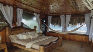 Un lit en bois avec un hamac, un plancher en bois et une vue sur la plage.