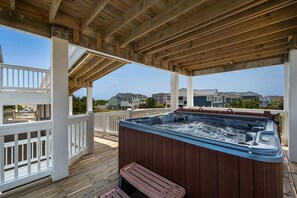A wooden deck with a hot tub, white railings, and a view of houses in the background.