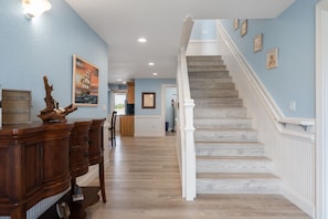 A spacious hallway with a wooden staircase, a dining area with a wooden table and chairs, and a kitchen area.