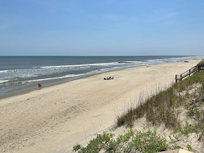 A beach with a wooden walkway leading to the water, sandy terrain, and sparse vegetation.