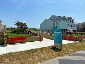 A coastal property with a wooden staircase leading to a house, a red bench, and a sign indicating beach access. - Atabey-Amazing Home! Private pool, 2 hot tubs, elevator, rec room, ocean views! (Corolla)