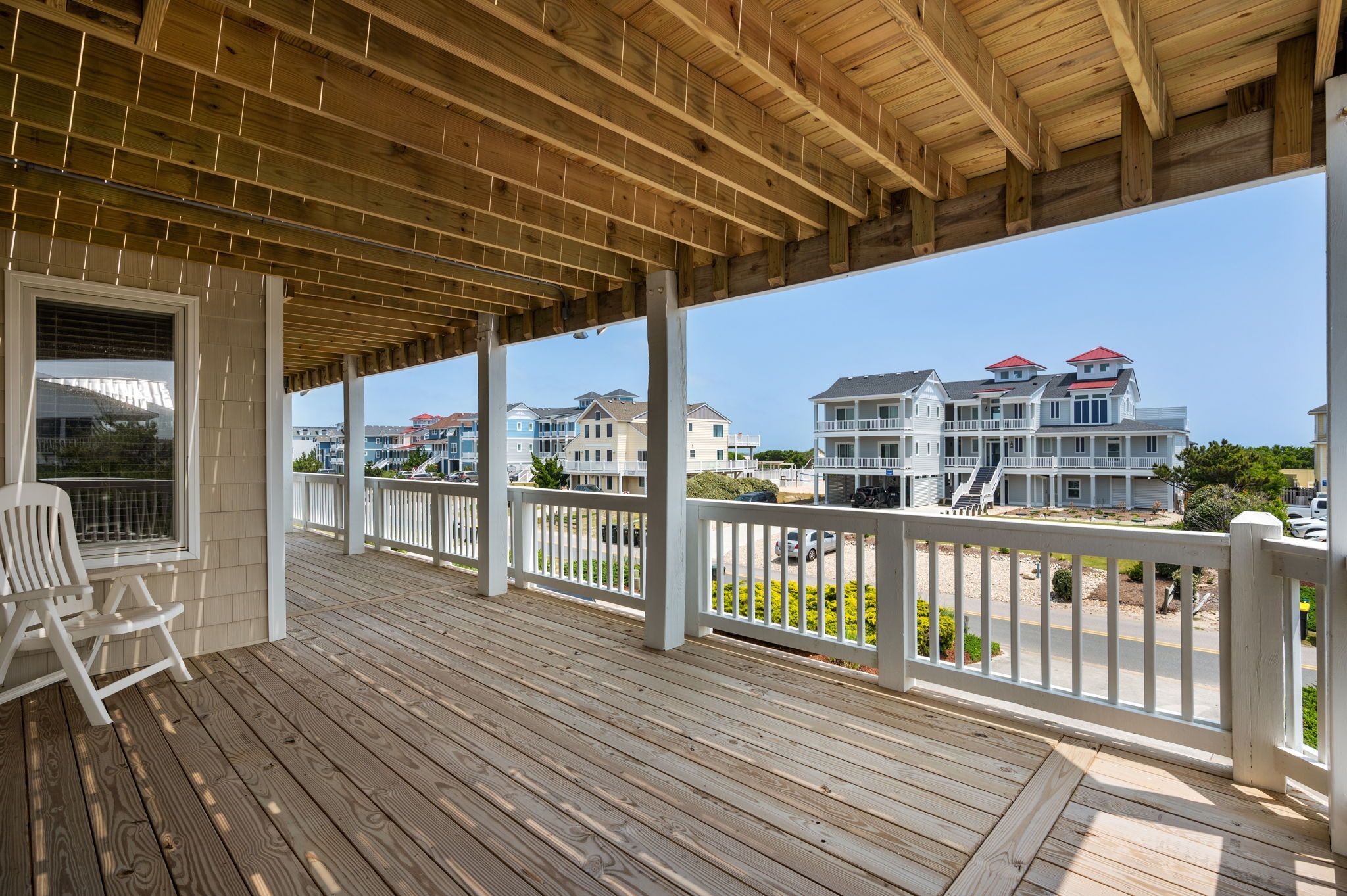 A wooden deck with white railings, a white chair, and a view of multi-story buildings in the background.