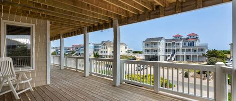 A wooden deck with white railings, a white chair, and a view of multi-story buildings in the background.
