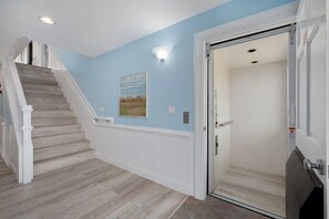 A hallway with a wooden staircase, a light blue wall, and a door with a glass panel. - Atabey-Amazing Home! Private pool, 2 hot tubs, elevator, rec room, ocean views! (Corolla)