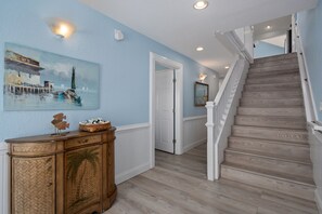 Un couloir avec un escalier en bois, un tableau accroché au mur et un meuble.