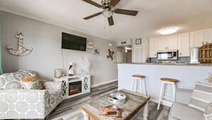 Ein Wohnzimmer mit Kamin, Deckenventilator, Küchenzeile mit Mikrowelle und zwei Barhocker.