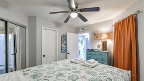 Ein Schlafzimmer mit Bett, Deckenventilator, Kommode und einer Tür zu einem anderen Raum.