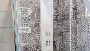 En brusekabine med kontrolpanel, glasdør og mønstrede fliser.